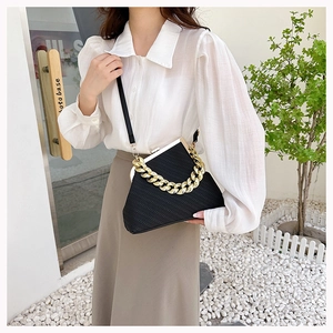 Detail view of black shell bag with thick gold chain handle and metal frame closure
