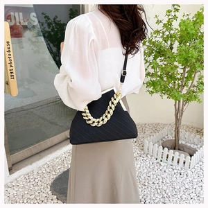 Detail of black trapezoid shell bag with textured fabric and gold chain handle decoration