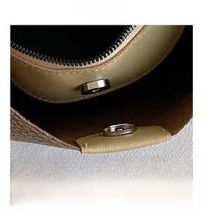 Macro detail of the magnetic snap closure and zipper on a beige textured PU leather bag