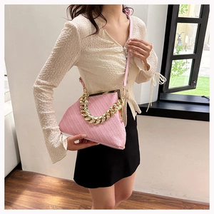 Pink shell handbag with woven texture and bold gold chain handle detail close-up
