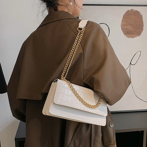 Sac bandoulière blanc à motif crocodile et chaîne dorée porté par un mannequin