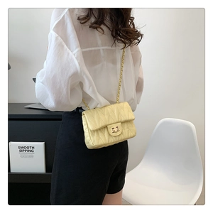 Detail of light yellow quilted crossbody bag with gold chain strap worn by a model