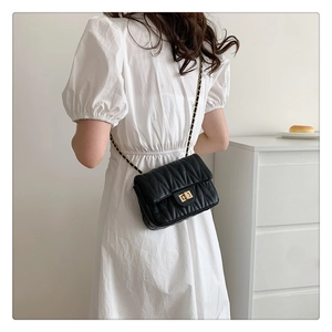 Detail of black quilted chain bag with gold twist lock on woman shoulder in bright room
