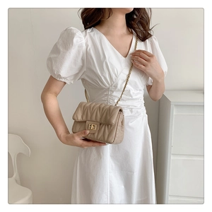 Detail of beige quilted flap bag with V-shaped stitching and gold chain strap shown on model