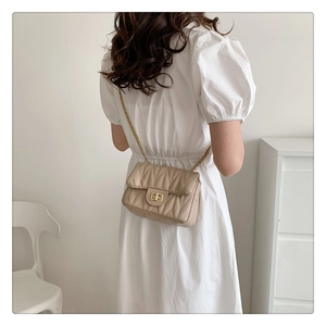 Detail of beige quilted shoulder bag with gold chain strap on a white dress