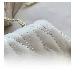 Close-up of white quilted shoulder bag showing precise V-stitch and gold chain strap