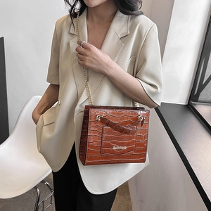 Sac fourre-tout marron à motif crocodile et chaîne dorée porté par un mannequin