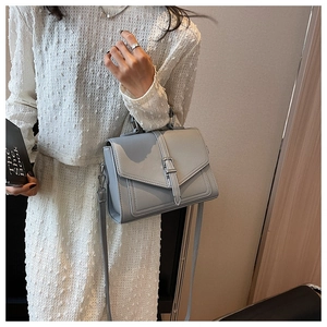 Detail of grey pebble-textured crossbody bag with silver buckle and thin strap