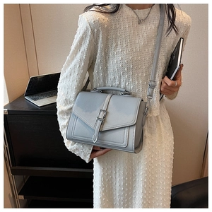 Detail of light blue crossbody square bag with top handle and textured litchi leather