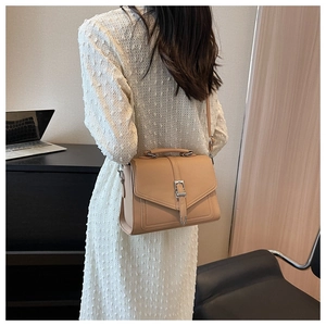 Side view of a khaki leather shoulder bag with silver hardware on a model in an office
