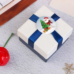 Square Christmas gift box with blue ribbon and Santa Claus sealing sticker on white tabletop