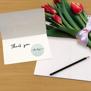 White Thank You greeting card with translucent cover and sticker on a wooden table