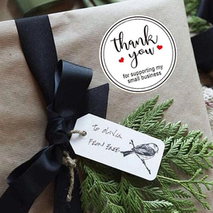 White round Thank You stickers with red hearts on a kraft gift box with black ribbon