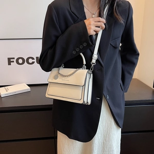 Borsa a tracolla beige alla moda con catena indossata da una modella in uno studio