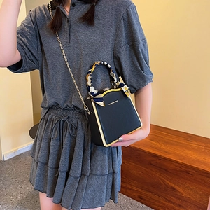 Elegant black box bag with gold metal frame and decorative silk scarf handle on crossbody strap