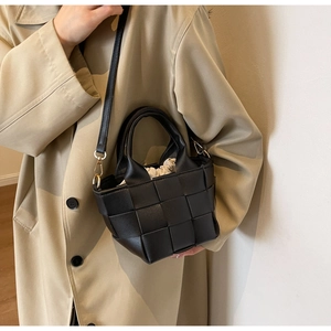 Dettaglio mini borsa intrecciata nera con sacchetto interno crema indossata su un trench