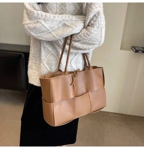 Close-up of brown woven leather tote bag carried by a model in a minimalist setting