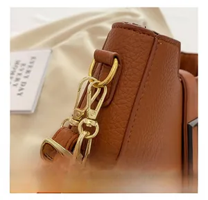 Dettaglio delle fibbie in metallo dorato e catena su borsa in pelle marrone litchi