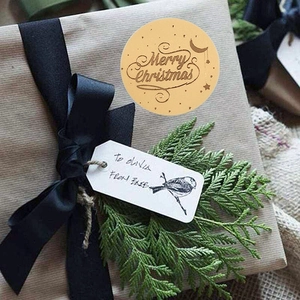 Brown gold-stamped Merry Christmas stickers on kraft gift box with pine branch decor