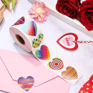 Roll of heart-shaped rainbow stickers on pink envelope with roses for gift wrapping