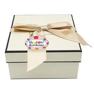 Ruban doré champagne élégant sur boîte cadeau ivoire avec autocollant Joyeux Anniversaire