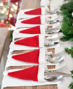 Set of 6 mini red plush Santa hats used as festive cutlery holders on a wooden table