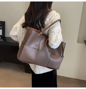Rear view of a model carrying a large brown woven leather tote bag in a minimalist room