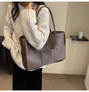 Detail of deep brown woven leather tote bag with matte texture and large weave pattern