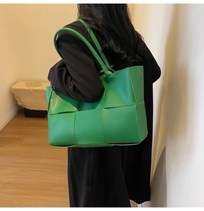 Detailed view of large green woven leather tote bag shown on model for shoulder carry