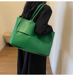 Close-up of bright green woven leather tote bag carried on shoulder with black blazer