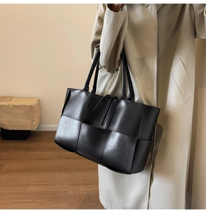 Detail of black woven leather tote bag featuring wide-weave design and dual top handles