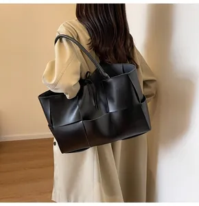Detailed view of black woven tote bag with large leather strips on a trench coat model