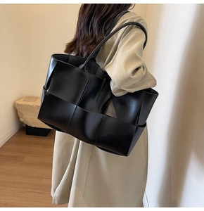 Rear view of a model carrying a large black woven leather tote bag in a minimalist room