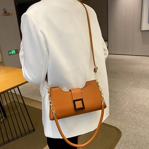 Borsa sottobraccio caramello con fibbia nera e catena dorata su un blazer bianco elegante