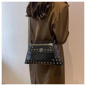 Detail of vintage black studded handbag with chain strap worn over a brown coat