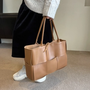 Caramel brown woven leather tote bag with long handles in a minimalist interior setting