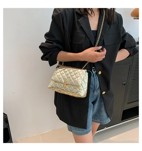 Close-up of golden quilted crossbody bag featuring a metallic turn-lock and chain strap