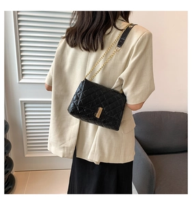 Detail of black quilted leather shoulder bag with gold chain strap and square metal clasp