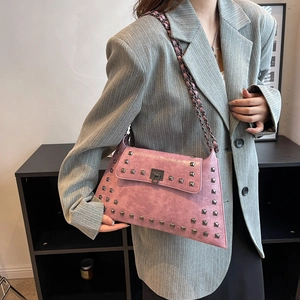 Pink punk shoulder bag with rivets and chain strap, shown on model in grey blazer