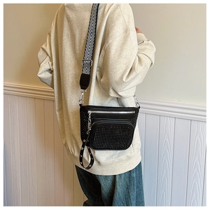 Detail of black rivet crossbody bag with silver studs and geometric stripe strap