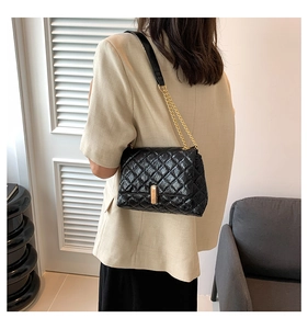 Detail of black quilted leather shoulder bag with gold chain strap and metal buckle