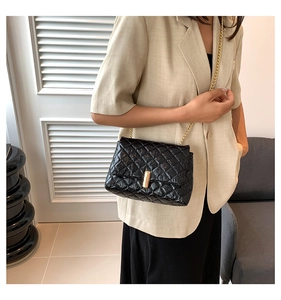 Detail of glossy quilted crossbody bag with gold chain strap and metal clasp on beige blazer