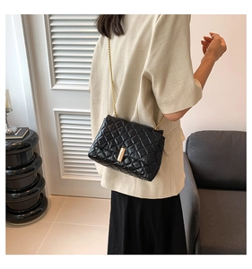 Detail of black quilted leather chain bag with gold buckle on a stylish model
