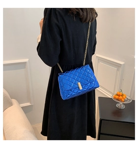 Detailed view of glossy blue quilted crossbody bag with gold chain strap on model