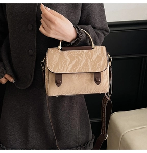 Detail of khaki textured handbag with golden ring handle and branded wide strap