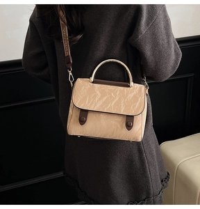 Close-up of khaki pleated leather bag featuring dark brown trim and branded woven strap