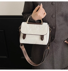 Detail of white marble textured handbag with gold metal handle and wide logo strap