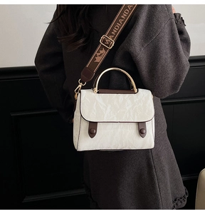 Detail of white wrinkled leather handbag with gold metal handle and logo strap