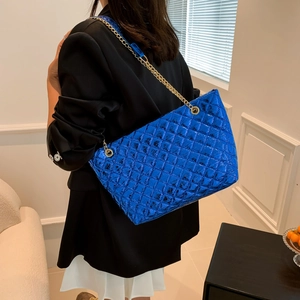 Blue quilted tote bag with gold chain strap shown on model in urban fashion setting