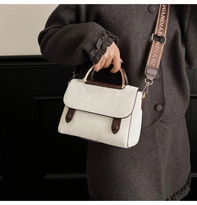Detail of cream PU leather handbag featuring dark brown trim and golden metal handle